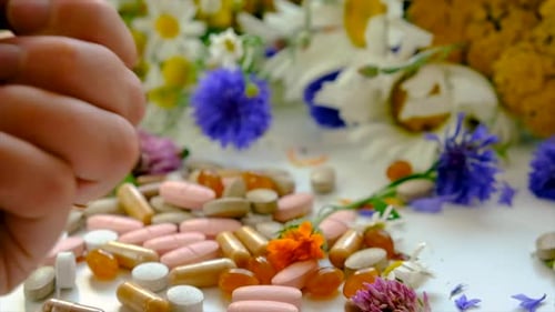 Hand Drops Pills on Table with Flowers