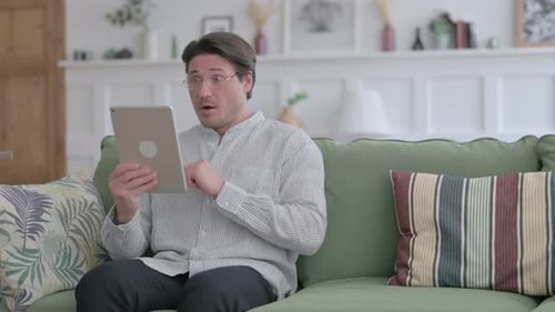 Man Reacts to Tablet While Sitting on Couch