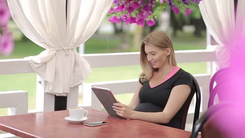 Smiling girl spending time in a street cafe using digital tablet