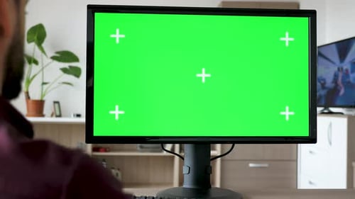 Unrecognisable Man Looking at Modern Personal Computer with Big Green Screen Chroma Mock Up