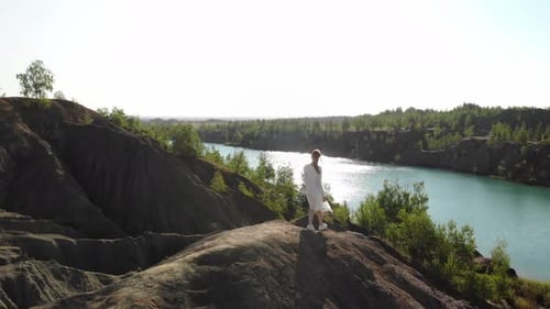 Schöne schlanke Frau in langem weißen Kleid nähert sich dem Rand des Abgrunds und breitet ihre Arme zur Seite