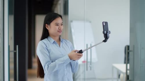 Young Asian Lady Blogger Recording Video on Smartphone Waving Hand and Talking to Device Carrying