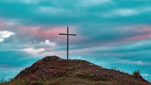 Iron Christian cross on a rocky hill. Colorful clouds in motion at sunset.