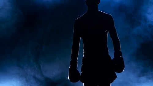 Un boxeur sort dans la fumée et fait preuve de muscles