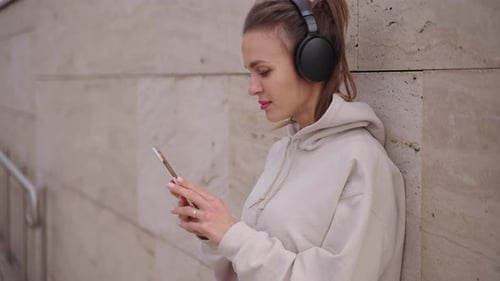 Woman with Headphones Using Phone by Wall