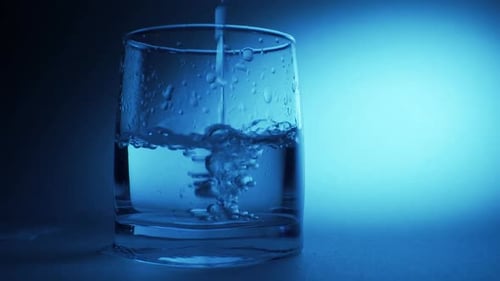 Water Pours into Glass in Blue Light