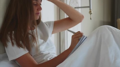 Young Woman Writing Notes to Diary After Awake in Bedroom at Home