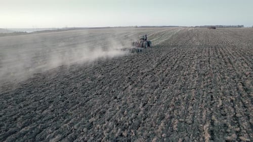 Drone Tracking Shot of Farming Tractor Plowing Dry Field After Collecting Harvest Pillar of Dust