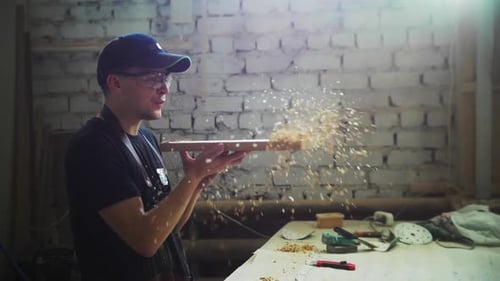 Carpentry Workshop a Man Worker Blows Sawdust Off a Wooden Board