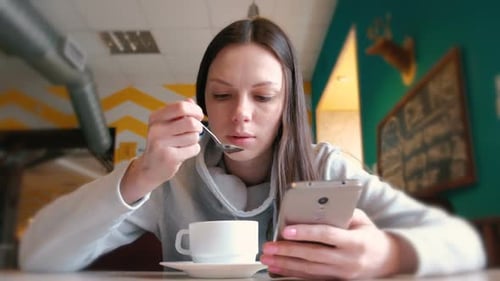 Young Woman Using Phone While Drinking Coffee Indoors