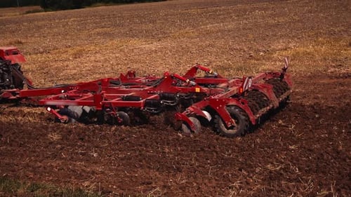 Tractor with disk harrow system plowing ground on cultivated farm field closeup. Cultivated