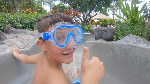 A boy plays on a waterslide water slide in a pool at a hotel resort.