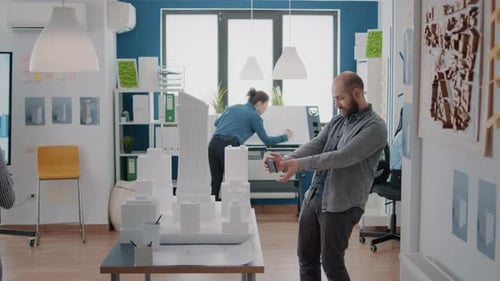 Man Using Smartphone to Design Building Model and Construction Layout with Maquette in Office