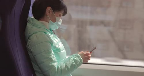 Woman Wears Mask and Uses Smartphone on Train