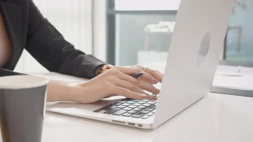 Closeup hands of young woman typing keyboard on laptop computer and writing note in the office.