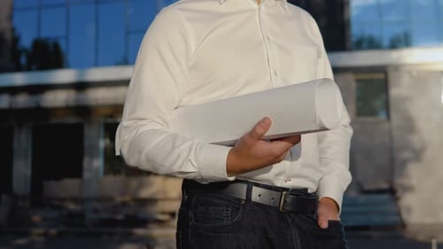 Ein Ingenieur in weißem Hemd und Helm arbeitet am Bau eines modernen Glasgebäudes und