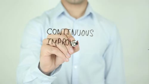Man Writing Continuous Improvement on Glass Surface
