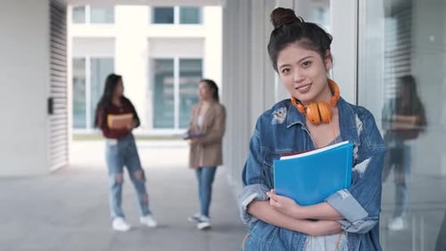 Portrait of an Asian college student holding folders and looking at the camera while standing