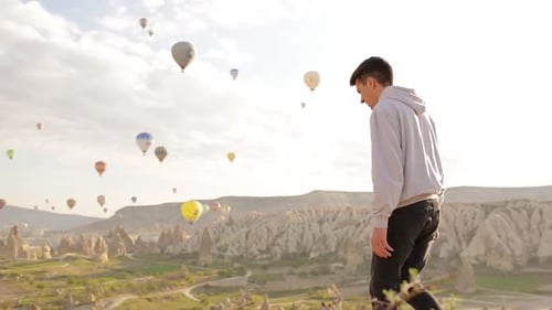 Young Adult Watching Hot Air Balloons in Valley