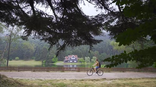 Cyclist Riding Beside Scenic Lake on Cloudy Day