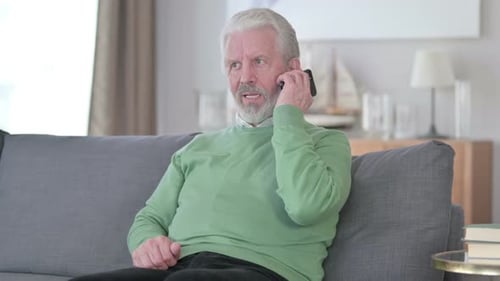 Senior Man Answering Mobile Phone Call on Couch