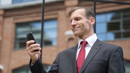 Smiling Businessman Using Mobile Phone Outside Office Building