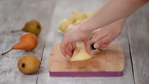 Woman's Hands Cutting Pear on Wooden Cutting Board.