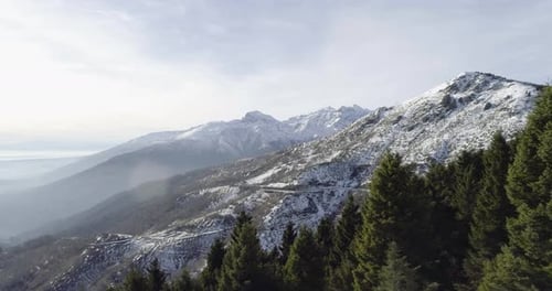 Forward Aerial Drone Flight Establisher Over Snowy Forest Woods with Mountains in Winter