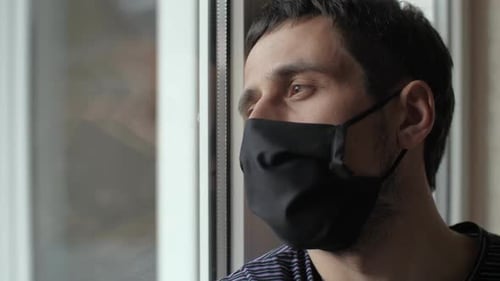 Homem triste com máscara protetora olha para a janela