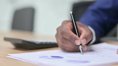 Close-Up of Person Writing on Financial Documents