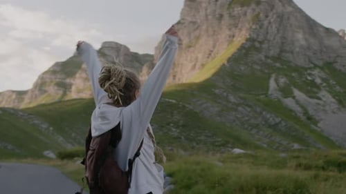 Happy millennial woman with dreadlocks spinning against mountain valley at sunset in Montenegro.