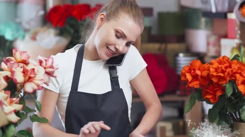 Florist Woman Discusses the Order By Talking on Obile Phone in a Flower Shop Working Online Flower
