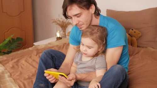 Father and Daughter Watch Smartphone on Bed