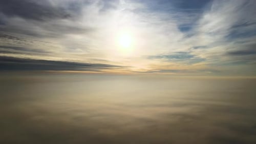 Aerial view of vibrant yellow sunrise over white dense clouds with blue sky overhead