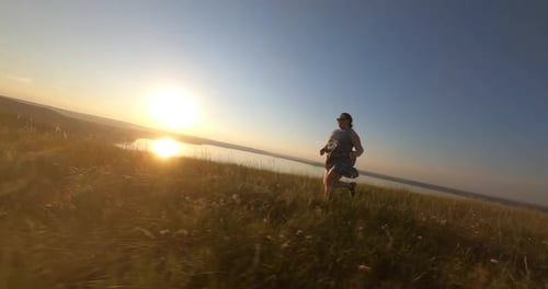 Panorámica aérea con Zumbido FPV de mujer alegre corriendo por el campo de hierba verde al atardecer