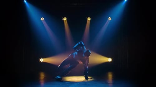 Young Sporty Guy Dancing Break Dance on the Background of Studio Lighting. Silhouette Dancer Man