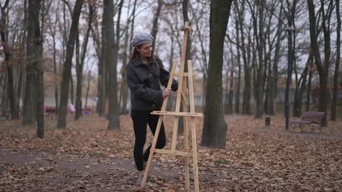 Wide Shot Portrait of Confident Young Caucasian Woman Placing Easel Outdoors Crossing Hands Smiling