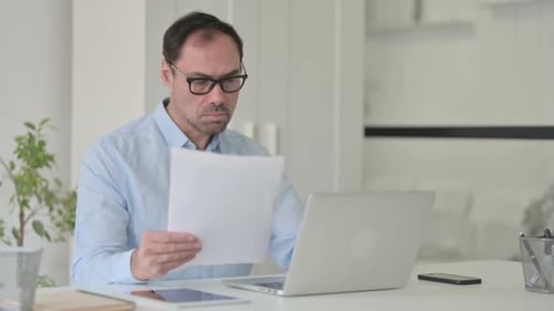 Man Celebrates Success Reading Document at Desk
