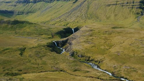 Drone Flight Over a Waterfall Descending in the Middle of the Green Hills in Iceland Summertime