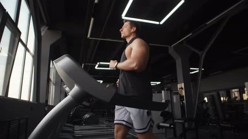 Athletic Man Wearing Headphones Does Cardio in Gym on Treadmill Side View