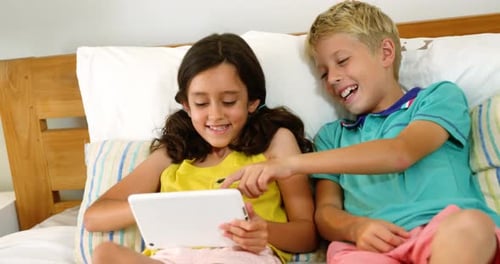 Siblings using digital tablet in bedroom