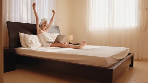 Woman Celebrating Success with Laptop in Bed