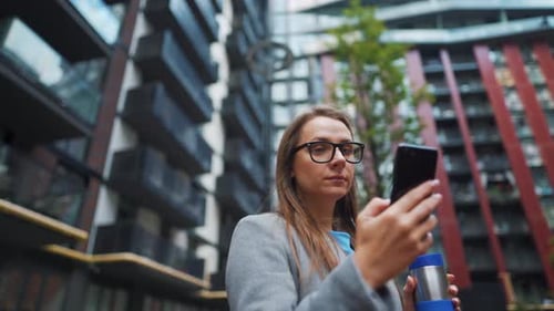 Formally Dressed Woman Walking Down the Street in a Business District with Coffee in Hand and Using