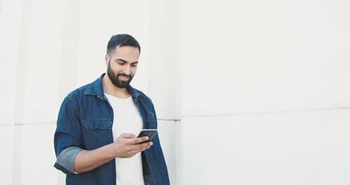 Man Smiling at Phone Outdoors in Urban Setting