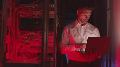Man Typing on Laptop in Server Room