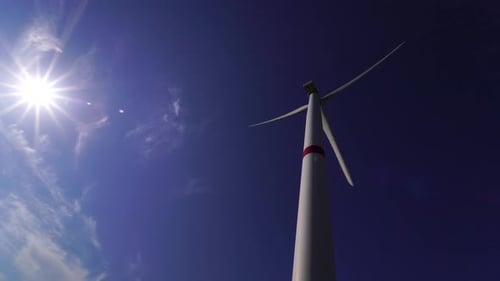 Blätter einer großen Windkraftanlage in einem Feld vor dem Hintergrund eines wolkenblauen Himmels am Horizont