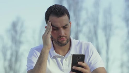 Frustrated Man Looks at Mobile Phone Outdoors