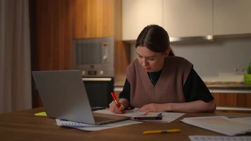 Portrait of a Woman Working Remotely in a Home Office at a Desk with a Laptop and Notes Data on a