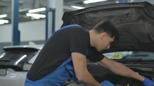 Side View of Concentrated Profesional Man Fixing Open Car Hood Auto Parts in Repair Shop