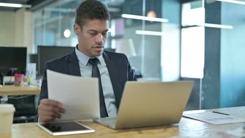 Young Adult Examining Papers at Office Desk